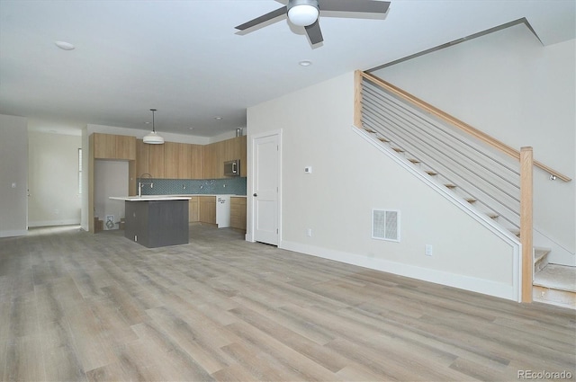 kitchen with light wood-type flooring, tasteful backsplash, ceiling fan, pendant lighting, and a center island with sink