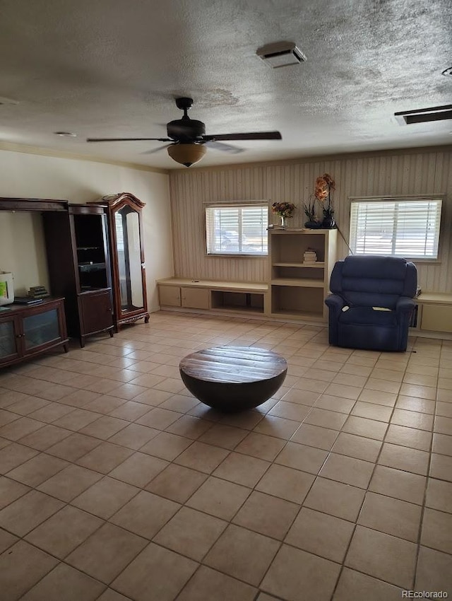 unfurnished living room featuring visible vents, a ceiling fan, a textured ceiling, wooden walls, and light tile patterned flooring