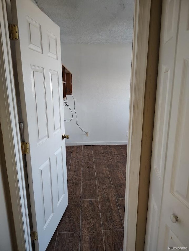 corridor with dark wood finished floors, baseboards, and a textured ceiling