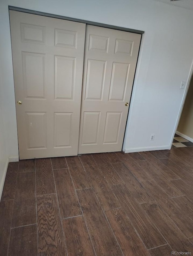 unfurnished bedroom featuring a closet, baseboards, and dark wood-type flooring