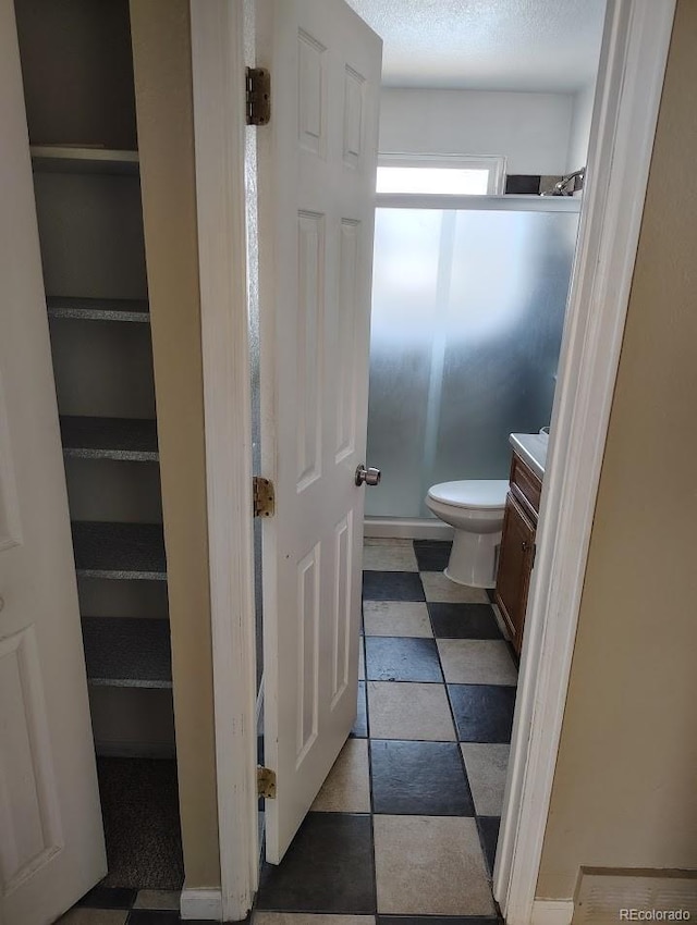 bathroom featuring tile patterned floors, toilet, vanity, and a shower with shower door