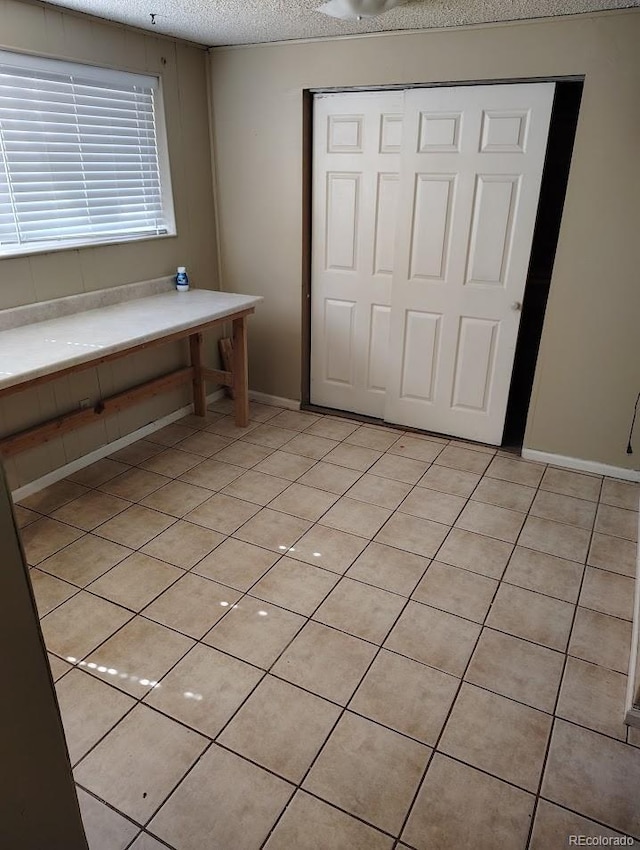 interior space with light tile patterned floors, baseboards, and a textured ceiling