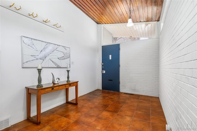 foyer entrance featuring visible vents, brick wall, dark tile patterned flooring, and wooden ceiling