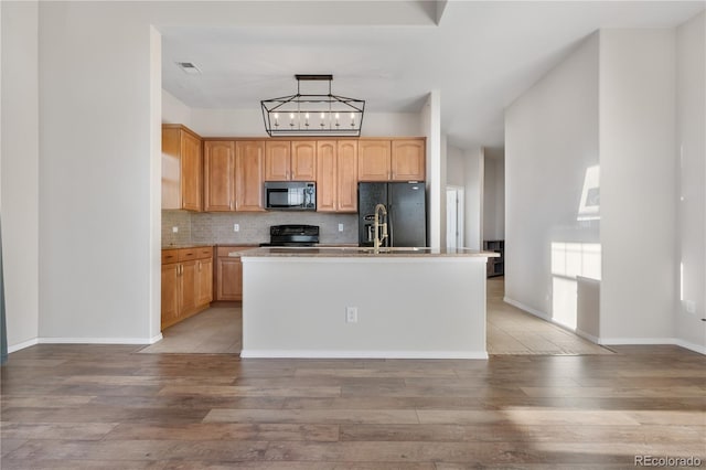 kitchen with tasteful backsplash, a center island with sink, black appliances, and light hardwood / wood-style flooring