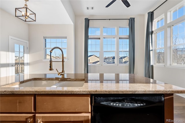 kitchen with sink, light stone countertops, black dishwasher, and a wealth of natural light