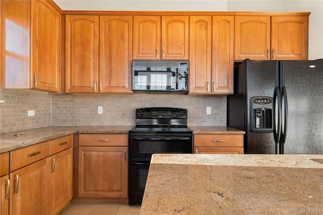 kitchen with decorative backsplash, light tile patterned floors, light stone counters, and black appliances