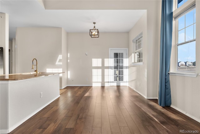 unfurnished living room with a notable chandelier, sink, and dark wood-type flooring