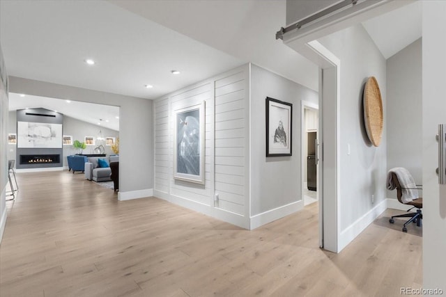 hall with lofted ceiling, a barn door, and light hardwood / wood-style floors