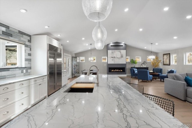 kitchen featuring built in refrigerator, white cabinetry, hanging light fixtures, and sink