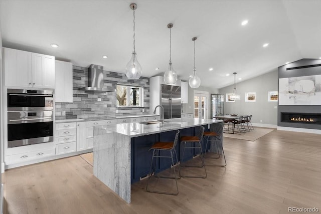 kitchen with white cabinetry, light stone counters, hanging light fixtures, a large island, and wall chimney range hood