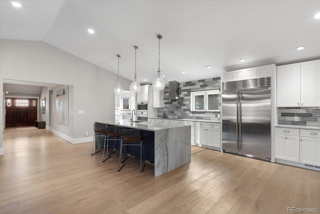 kitchen featuring white cabinetry, wall chimney exhaust hood, stainless steel built in refrigerator, and an island with sink