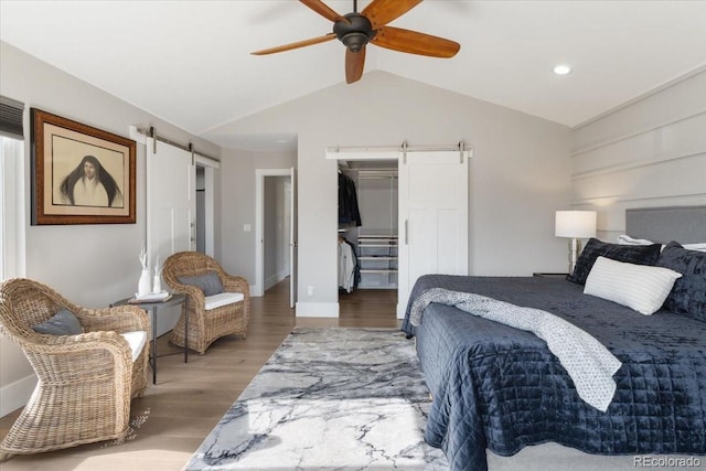 bedroom featuring vaulted ceiling, a barn door, wood-type flooring, and a spacious closet