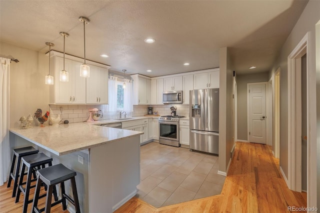 753 Edge Hill Dr, Woodland Park, CO 80863 - kitchen with a peninsula, appliances with stainless steel finishes, white cabinets, decorative backsplash, and a kitchen bar