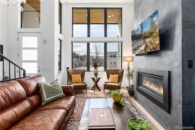 living room featuring stairs, wood finished floors, a high ceiling, and a glass covered fireplace