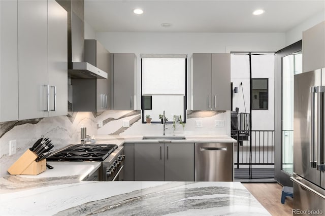 kitchen with wall chimney range hood, stainless steel appliances, gray cabinetry, and a sink