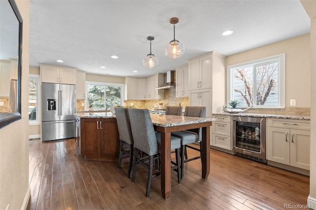 kitchen featuring high end fridge, wine cooler, wall chimney exhaust hood, and dark wood finished floors