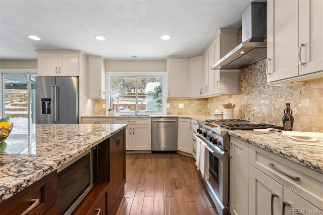 kitchen with dark wood-type flooring, a sink, light stone countertops, wall chimney exhaust hood, and high end appliances