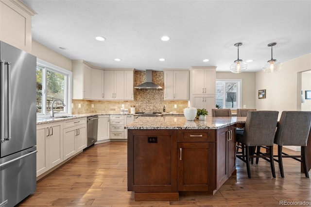 kitchen with appliances with stainless steel finishes, light wood-type flooring, backsplash, and wall chimney range hood