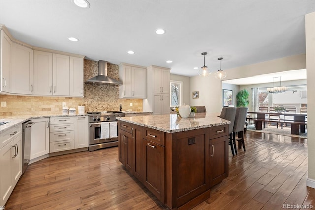 kitchen featuring wall chimney range hood, stainless steel appliances, wood finished floors, and a center island