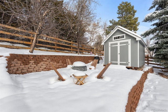 snowy yard featuring an outbuilding, a shed, and fence