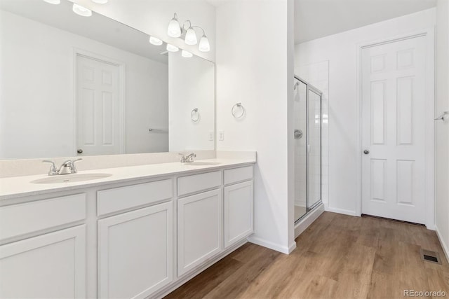 bathroom with wood-type flooring, a shower with door, and vanity