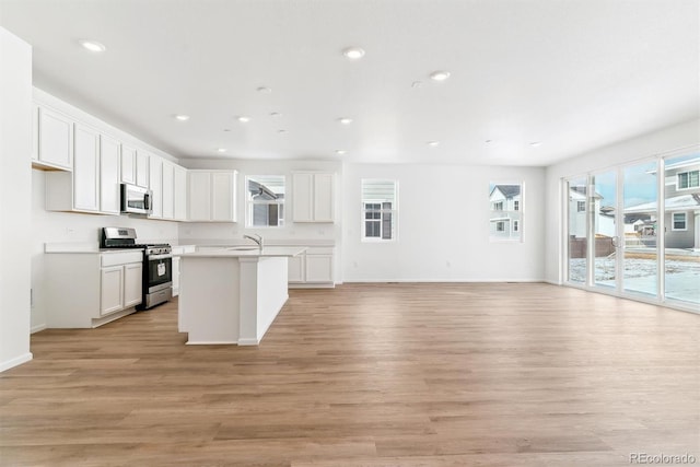 kitchen featuring sink, white cabinets, stainless steel appliances, a center island with sink, and light hardwood / wood-style flooring