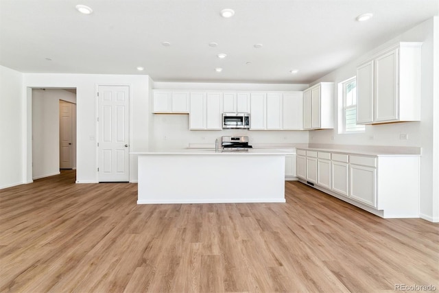 kitchen with white cabinetry, light wood-type flooring, a kitchen island with sink, and appliances with stainless steel finishes