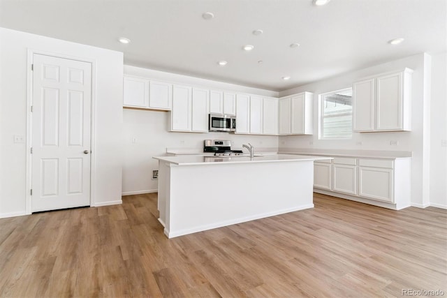 kitchen with white cabinetry, stainless steel appliances, an island with sink, and light wood-type flooring