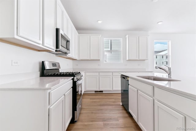 kitchen with white cabinetry, appliances with stainless steel finishes, sink, and light wood-type flooring