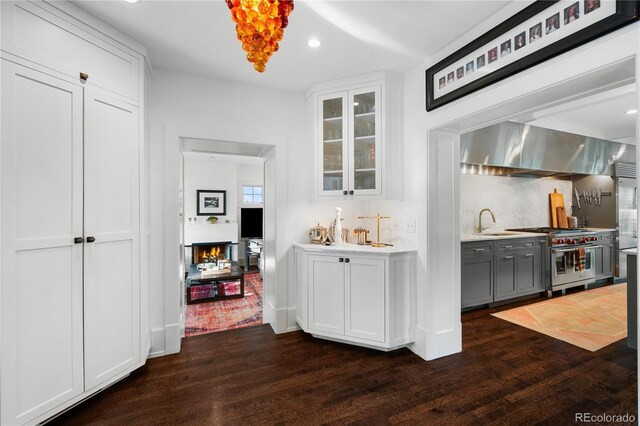 bar with high end stove, backsplash, dark wood-type flooring, and a sink