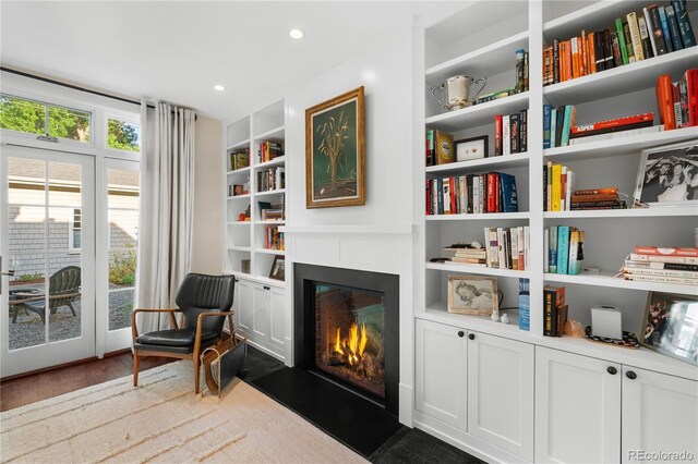 sitting room with recessed lighting, built in shelves, dark wood-style flooring, and a glass covered fireplace