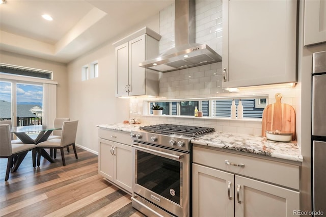 6362 Lythmore Grv, Colorado Springs, CO 80927 - kitchen featuring high end stainless steel range, wall chimney exhaust hood, light wood-style floors, baseboards, and a tray ceiling