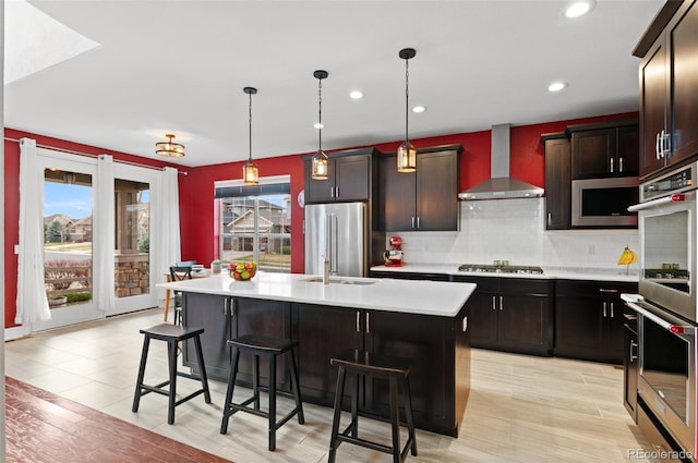 kitchen with light countertops, a breakfast bar area, appliances with stainless steel finishes, and wall chimney range hood