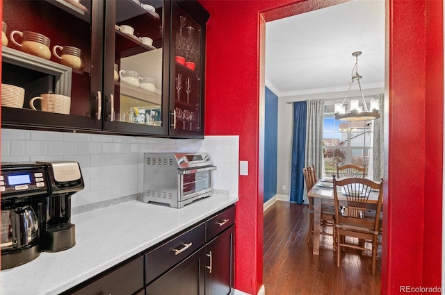 kitchen with a notable chandelier, baseboards, dark wood-style floors, crown molding, and backsplash