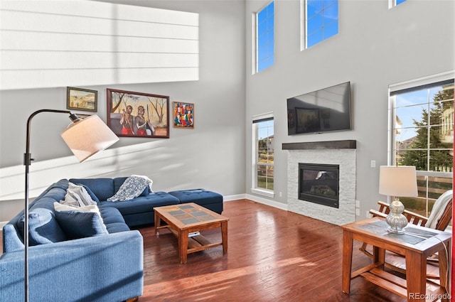 living area featuring plenty of natural light, a glass covered fireplace, wood finished floors, and a towering ceiling