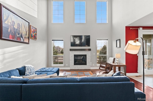 living area with a glass covered fireplace, a high ceiling, baseboards, and wood finished floors