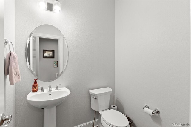 half bathroom with toilet, a sink, and baseboards