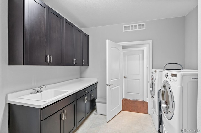 washroom with washing machine and dryer, a sink, cabinet space, and visible vents