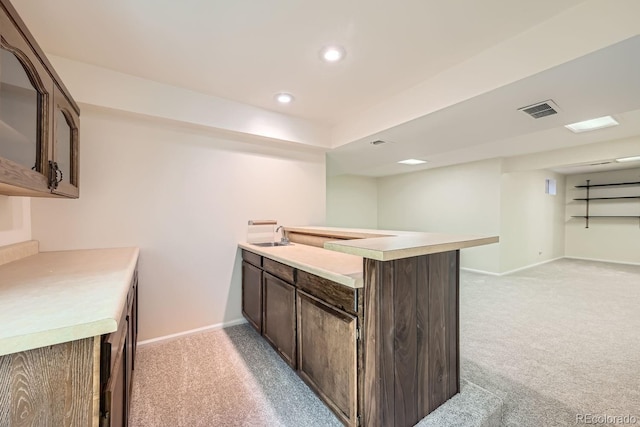 kitchen with kitchen peninsula, dark brown cabinetry, sink, and light colored carpet