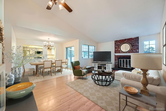 living room featuring ceiling fan with notable chandelier, light wood-type flooring, high vaulted ceiling, and a brick fireplace