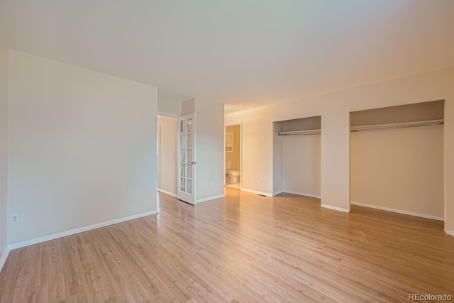 unfurnished bedroom with light hardwood / wood-style flooring and two closets