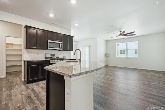 kitchen featuring sink, appliances with stainless steel finishes, a kitchen island with sink, light stone counters, and dark hardwood / wood-style flooring