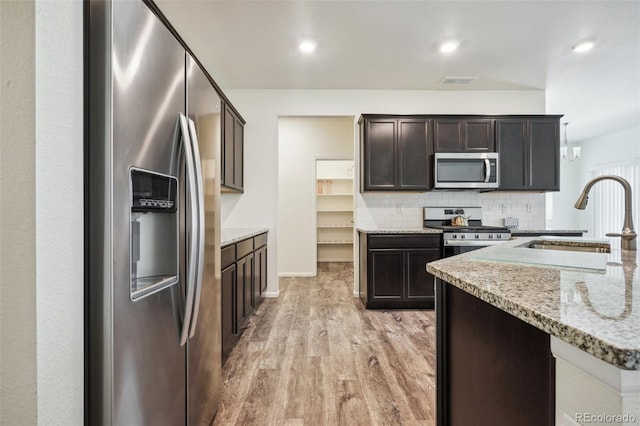 kitchen with sink, tasteful backsplash, stainless steel appliances, light stone countertops, and light hardwood / wood-style floors