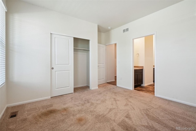 unfurnished bedroom featuring light carpet, ensuite bath, and a closet