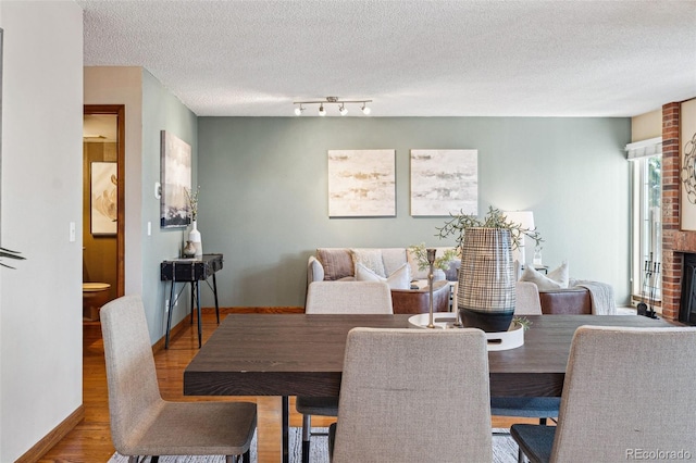 dining area with wood-type flooring, a brick fireplace, and a textured ceiling