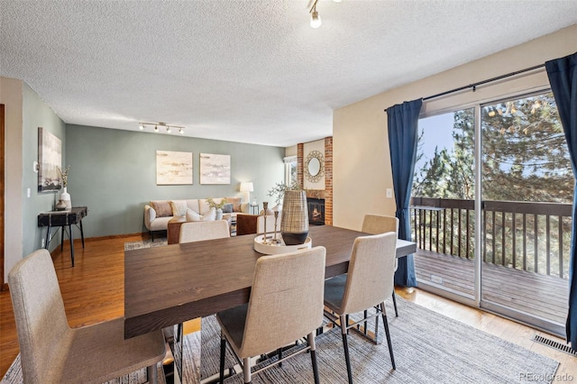 dining area with hardwood / wood-style flooring, rail lighting, a brick fireplace, and a textured ceiling