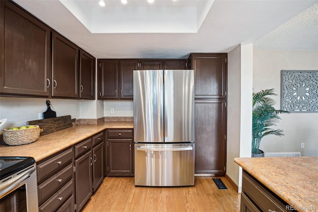 kitchen featuring dark brown cabinetry, light hardwood / wood-style flooring, stainless steel refrigerator, and a raised ceiling