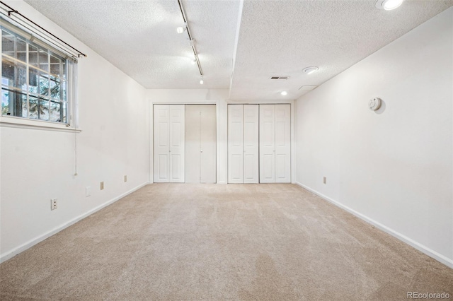 unfurnished bedroom with a textured ceiling, track lighting, multiple closets, and carpet