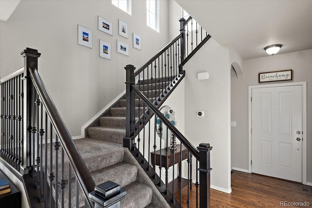 stairway with baseboards, arched walkways, and wood finished floors