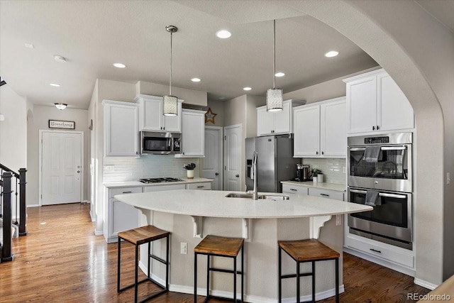 kitchen with arched walkways, an island with sink, backsplash, and stainless steel appliances